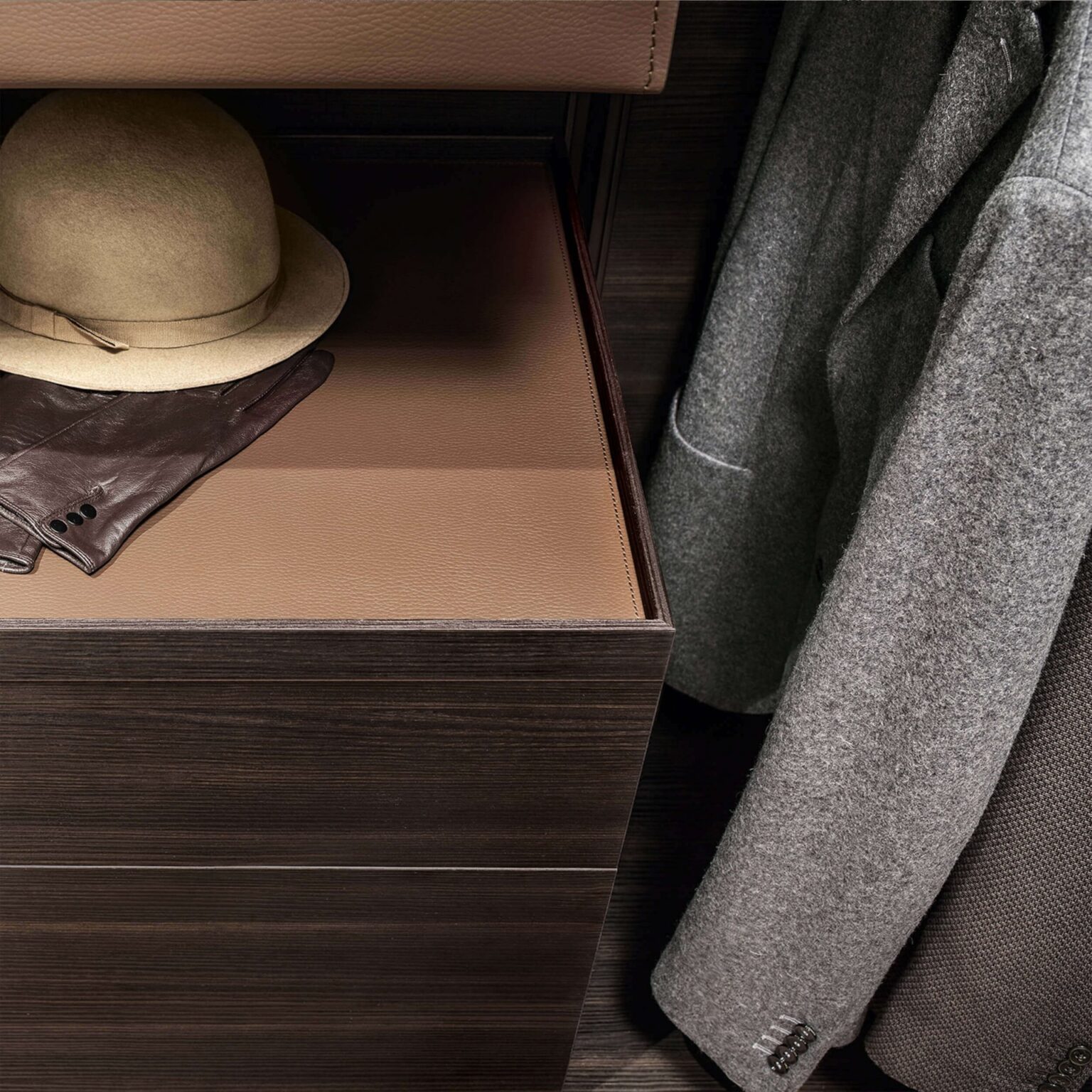 Detail van inloopkast met houten lade en leren bekleding naast hangende kleding in maatwerk garderobesysteem