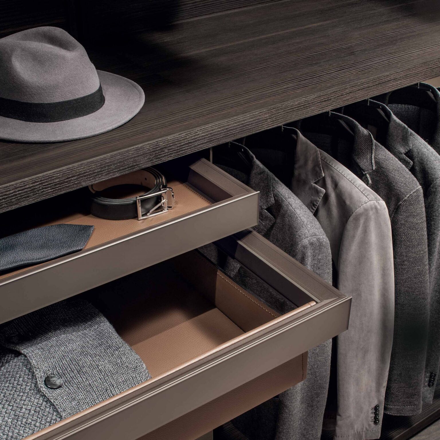 Detail van inloopkast met lade voor accessoires en hangende kleding in open garderobesysteem met verfijnde indeling