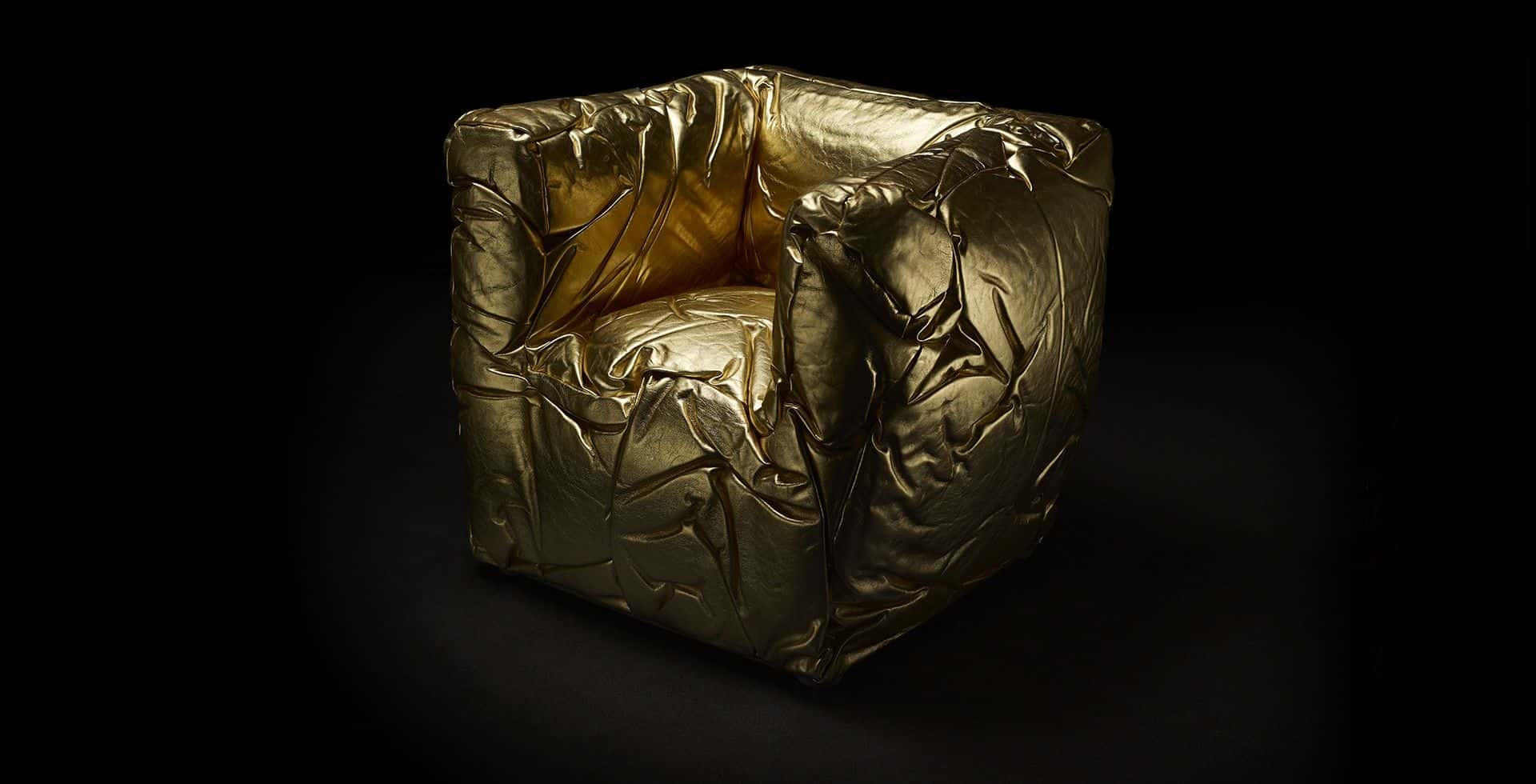 Sponge-armchair in een opvallende goudkleurige uitvoering. De leren bekleding, met karakteristieke onregelmatige rimpels, benadrukt het sculpturale en unieke karakter van de stoel. De luxe uitstraling en het artistieke vakmanschap komen duidelijk naar voren.