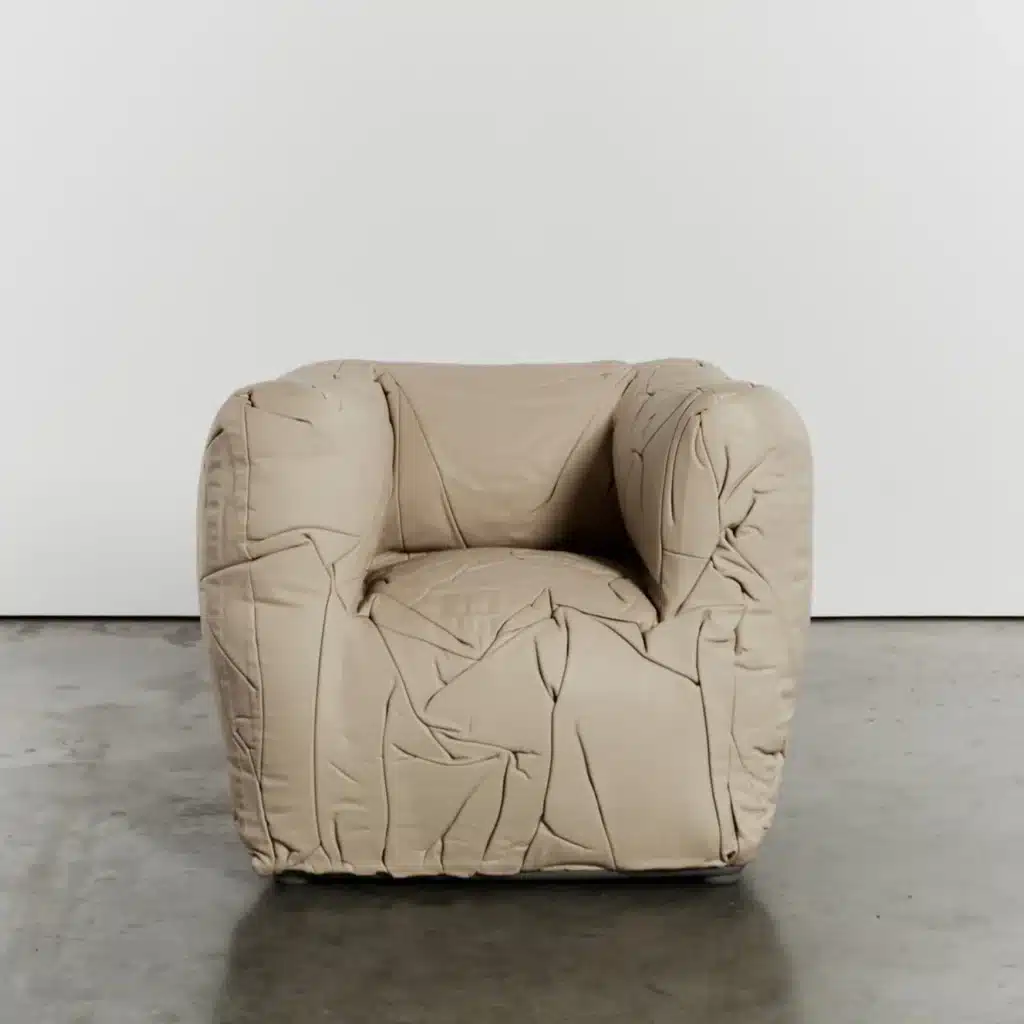 In deze afbeelding wordt de Sponge-armchair gepresenteerd in een zachte, beige kleur. De stoel staat in een minimalistische ruimte met een betonnen vloer, waardoor de textuur en vorm van de leren bekleding goed zichtbaar zijn. Deze variant van de stoel past perfect in moderne en strakke interieurs, waarbij comfort en esthetiek hand in hand gaan.