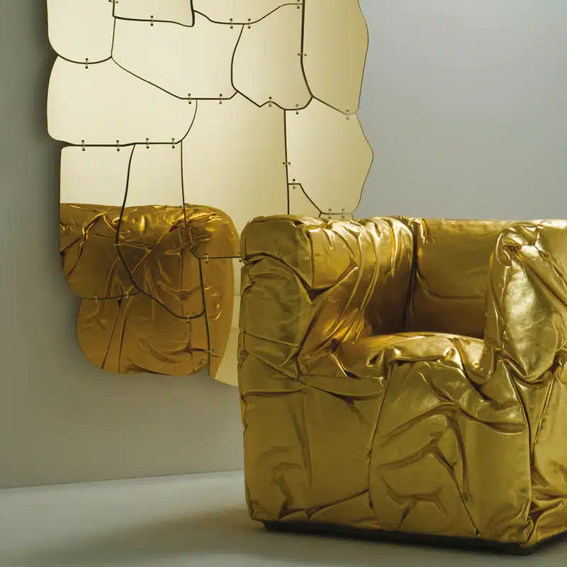 Deze afbeelding toont de Sponge-armchair in een opvallende goudkleurige uitvoering. De leren bekleding, met karakteristieke onregelmatige rimpels, benadrukt het sculpturale en unieke karakter van de stoel. De luxe uitstraling en het artistieke vakmanschap komen duidelijk naar voren.