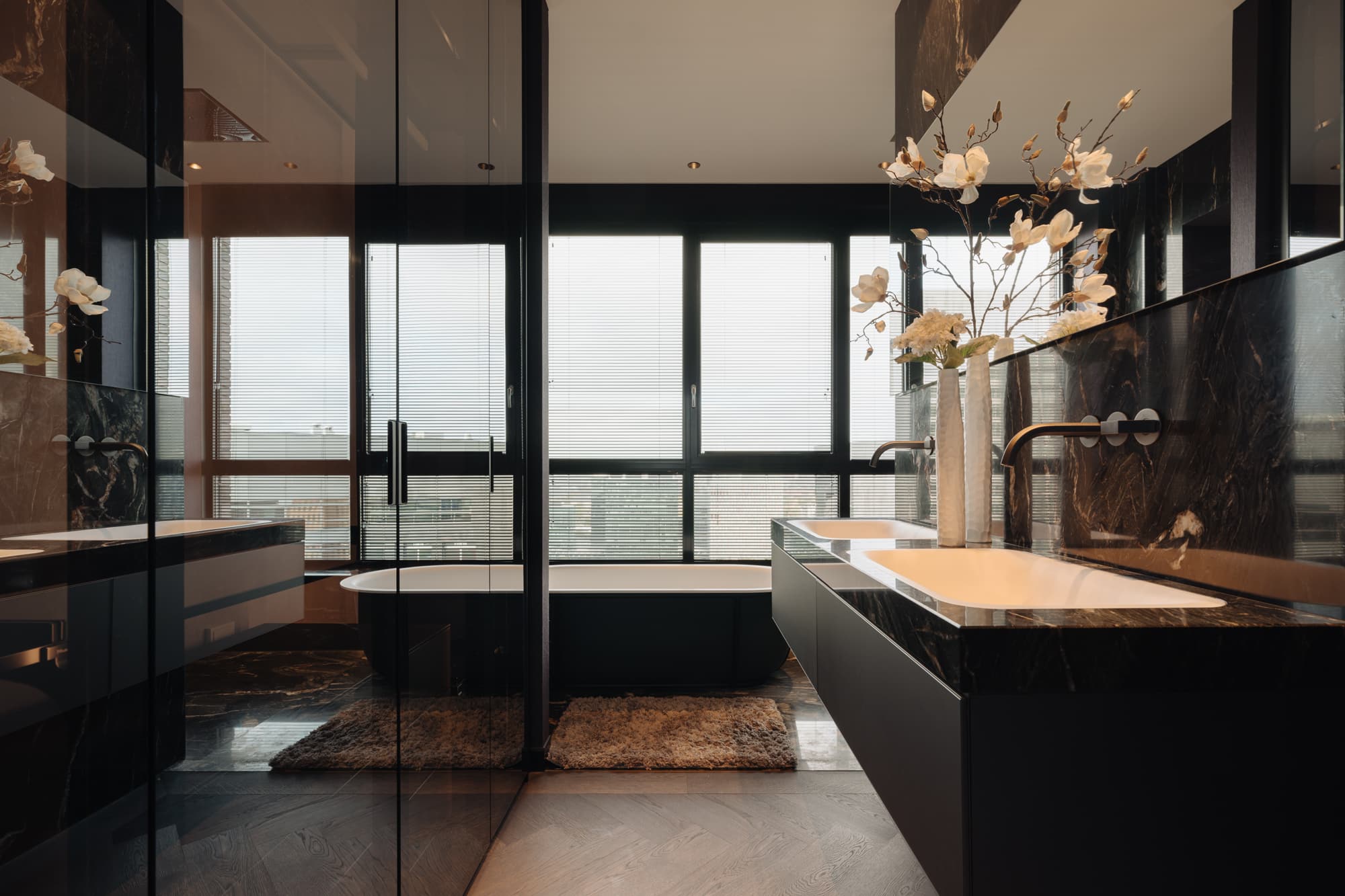 Badkamer met natuurstenen wanden en wastafelmeubel op maat, geïntegreerde kranen en glaswanden, ontwerp en realisatie Noctum