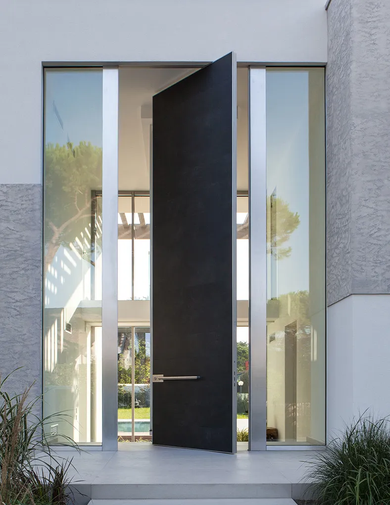 Oikos pivot veiligheidsdeur geïntegreerd in de entree van een moderne villa met hoge glaspartijen