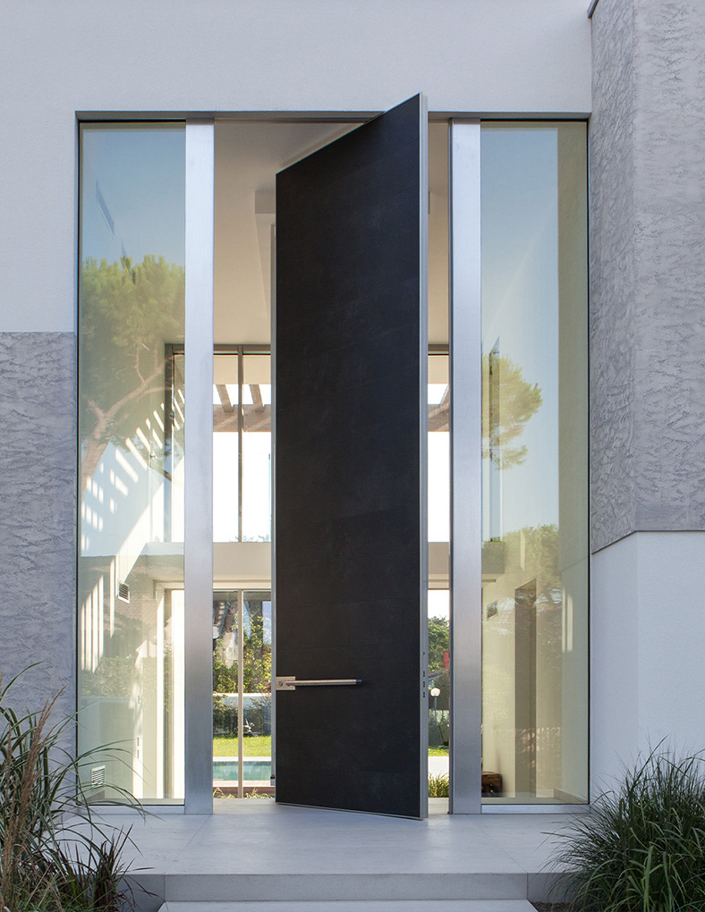 Architectonische pivotdeur van Oikos geïntegreerd in een moderne gevel met hoge glaspartijen.