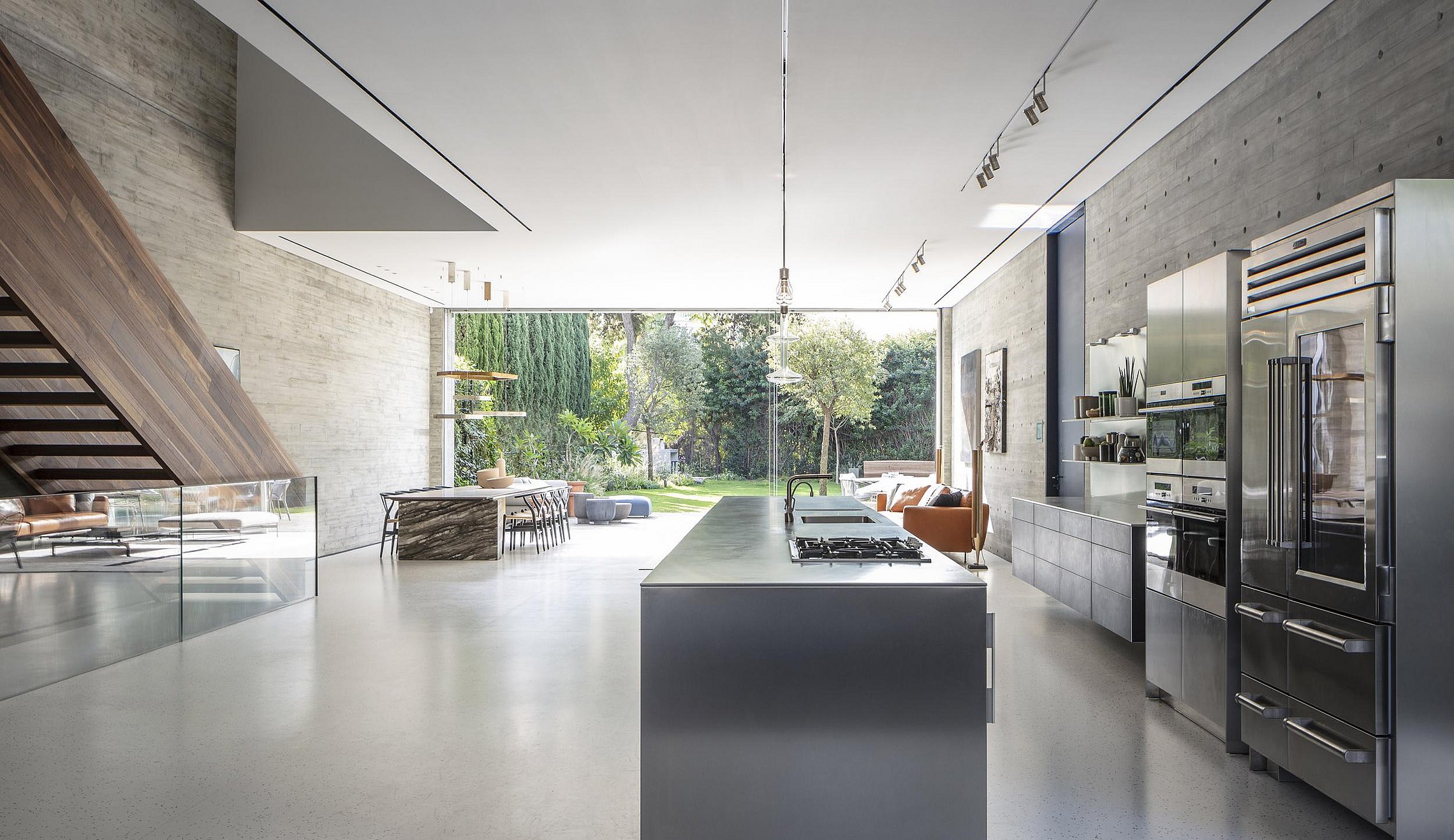 Open woonruimte met keuken, betonwand en zicht op tuin waarin interieur, architectuur en buitenruimte naadloos op elkaar aansluiten