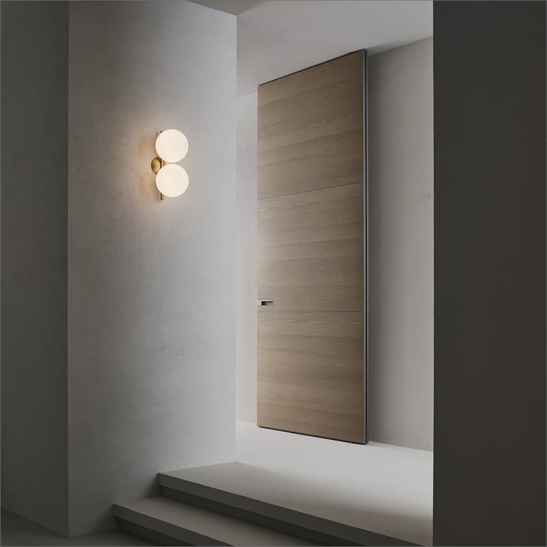Kamerhoge houten taatsdeur geïntegreerd in een coplanaire wand binnen een minimalistisch interieurproject