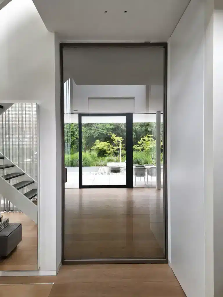 Rimadesio Air Pure taatsdeur in gesloten stand tussen hal en woonruimte, met doorzicht naar de tuin.