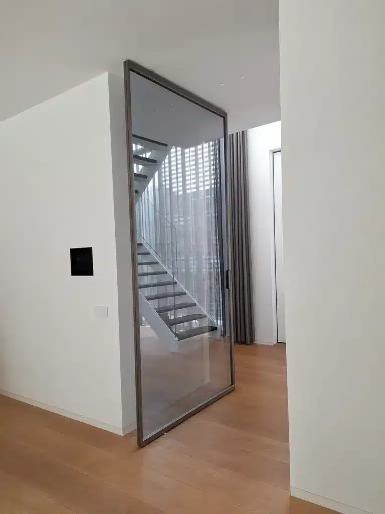 Rimadesio Air Pure taatsdeur in geopende stand tussen hal en woonruimte, met donkerkleurig aluminium profiel en helder glas.